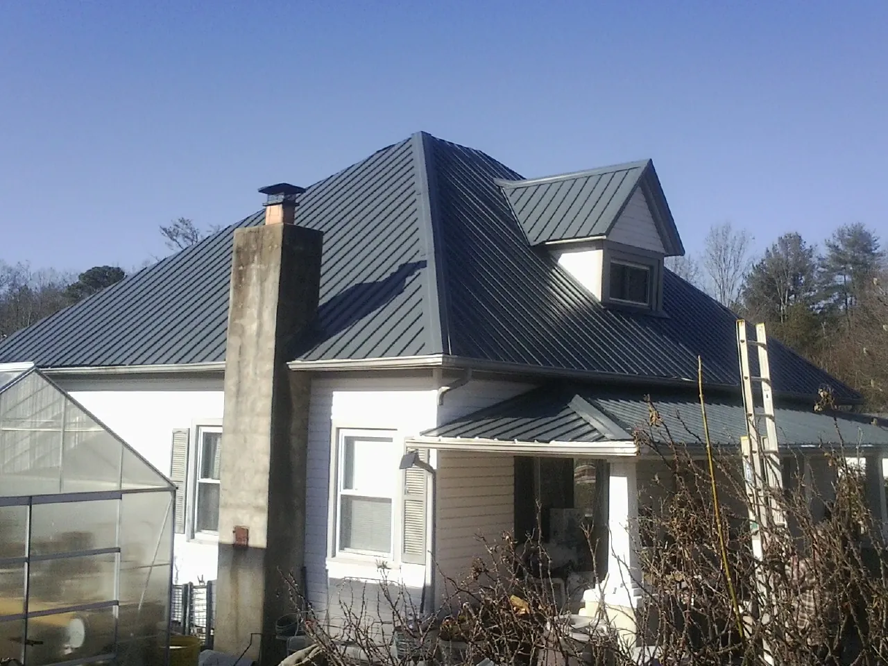 Dark blue standing seam metal roof on a white farmhouse with dormer — Slate & Tile Roof Repair by Roofing Brothers in Trion