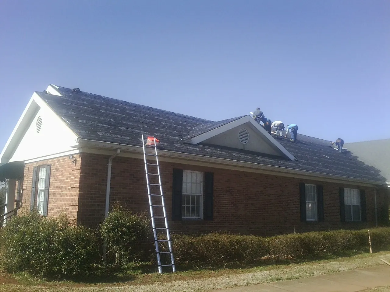 Crew tearing shingles off a brick ranch roof with a ladder set — Emergency Roof Repair work by our crew in Trion