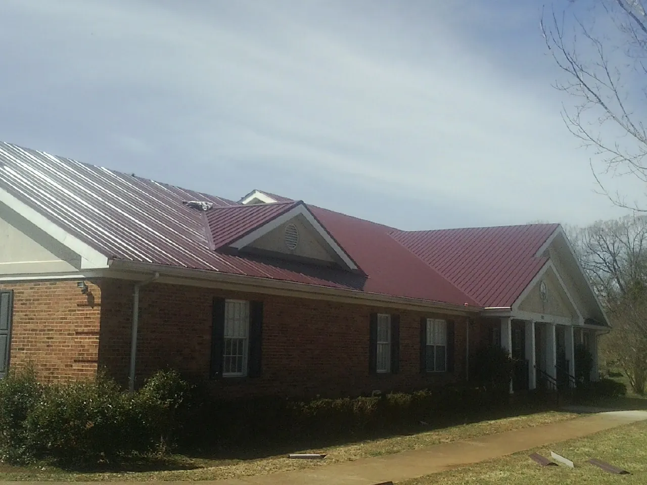 Red metal roof with gabled entries on a long brick building, from a Hail Damage Roof Repair job in Trion