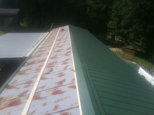 Old rusted panels beside newly installed green metal roofing — Wind Damage Roof Repair by Roofing Brothers in Trion