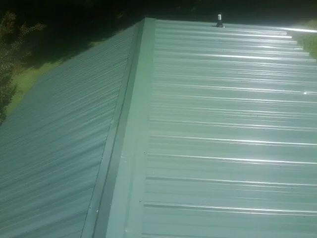 New green metal panels meeting at the ridge of a roof — Flat Roof Repair work by our crew in Trion